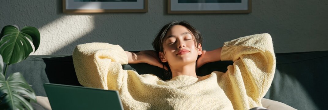 Woman leaning back with hands behind head on sofa in morning sun with laptop for relaxation and remote work break background and wellness lifestyle scene