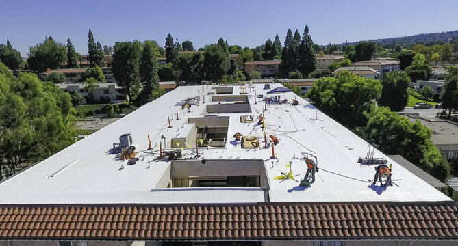 Tustin, CA, USA - 16 September 2026: Aerial view of workers installing solar panels on the flat roof of an apartment building under a clear blue sky.