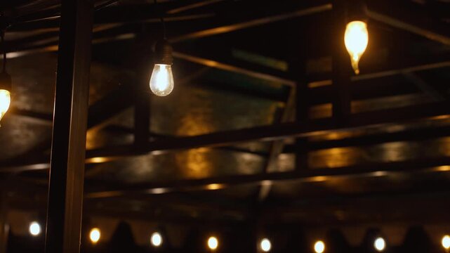Decorative string light bulbs hanging from a dark wooden ceiling structure, creating a warm and inviting glow for a party, wedding, or backyard gathering on a cozy evening