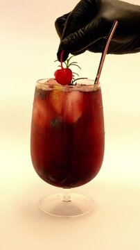 Gloved Hand Placing Maraschino Cherry Garnish on Cold Red Fruit Cocktail with Ice and Rosemary