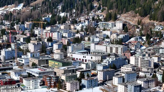 tower crane rises above dense davos rooftops construction site white church clock tower stands nearby alpine chalets climb forested hillside snowcapped ridgeline fills horizon graubunden switzerland