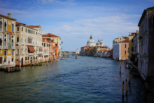 The Grand Canal in Venice stretches toward a domed basilica under a bright blue sky, lined with historic palaces.