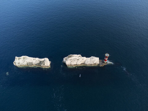 Isle of Wight, United Kingdom - 22 July 2021: Aerial view of The Needles, a row of three distinctive chalk stacks rising out of the sea, with a red and white lighthouse.