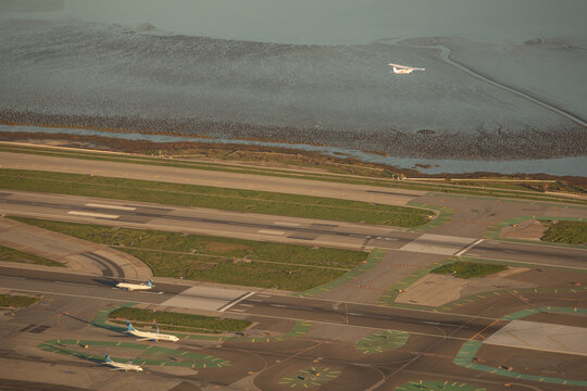 San Francisco, United States - 13 January 2026: Aerial view of San Francisco International Airport with airplanes on the tarmac and a small aircraft flying over the mudflats.