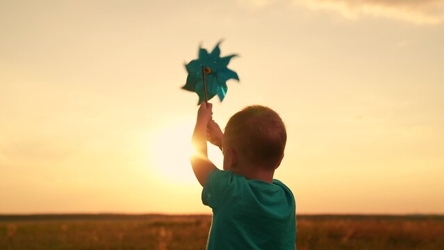 Child childhood. Family outing, nature. Kid boy runs through summer field holding toy pinwheel, sunny day. Happy child plays with toy pinwheel outdoors. Child nature. Child son, dream in park sunset