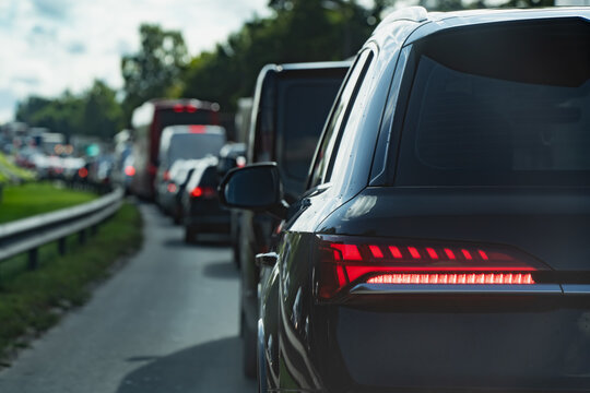 A line of cars and commercial vehicles queues behind a vehicle with illuminated rear lamps, illustrating traffic congestion and the demands of everyday road transport