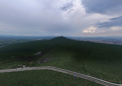 Santiago de Queretaro, Queretaro, Mexico - 14 September 2026: Aerial view of Parque Nacional El Cimatario, a green hill with dense vegetation, a winding road, and the city skyline.