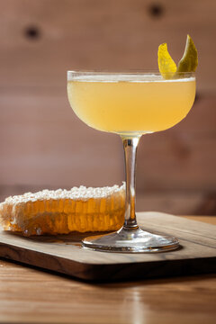 Elegant cocktail, the Bees Knees in coupe glass. Lemon twist adorns the rim. Warm wood table and honey comb garnish.