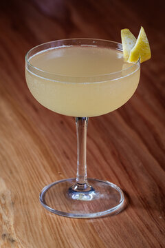 Elegant cocktail, the Bees Knees in coupe glass. Lemon twist adorns the rim. Warm wood table. Perfect for bar, lounge