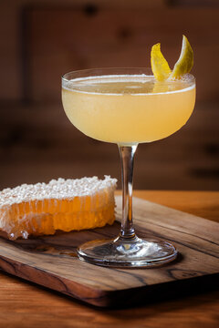 Elegant cocktail, the Bees Knees in coupe glass. Lemon twist adorns the rim. Warm wood table and honey comb garnish.