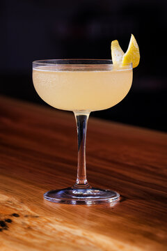 Elegant cocktail, the Bees Knees in coupe glass. Lemon twist adorns the rim. Warm wood table. Perfect for bar, lounge