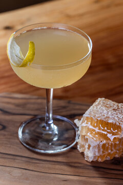 Elegant cocktail, the Bees Knees in coupe glass. Lemon twist adorns the rim. Warm wood table and honey comb garnish.