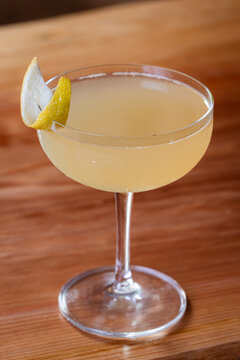 Elegant cocktail, the Bees Knees in coupe glass. Lemon twist adorns the rim. Warm wood table. Perfect for bar, lounge