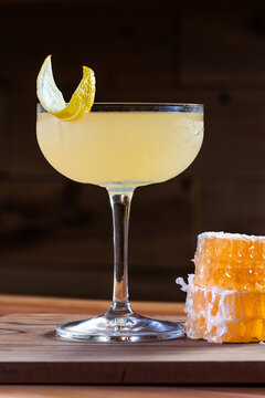 Elegant cocktail, the Bees Knees in coupe glass. Lemon twist adorns the rim. Warm wood table and honey comb garnish.