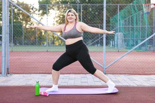 Overweight woman exercising on fitness mat at stadium