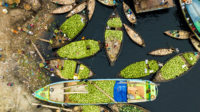 Dhaka, Bangladesh - 17 March 2023: Aerial view of Sadarghat with numerous wooden boats heavily laden with watermelons docked along the riverbank.