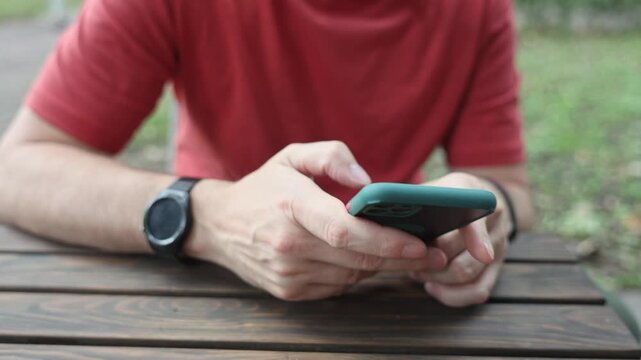 Close up of man hands using smartphone at wooden table outdoors in daylight
