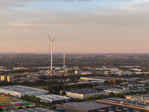 Genk, Vlaanderen, Belgium - 27 August 2026: Aerial view of the Genk-Zuid industrial area featuring wind turbines, warehouses, and logistics facilities under a soft evening sky.