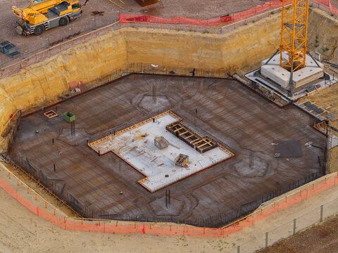 Genk, Belgium - 27 August 2026: Aerial view of the construction site foundation at Genk-Zuid with rebar reinforcement, a tower crane, and orange safety fencing in an industrial area.