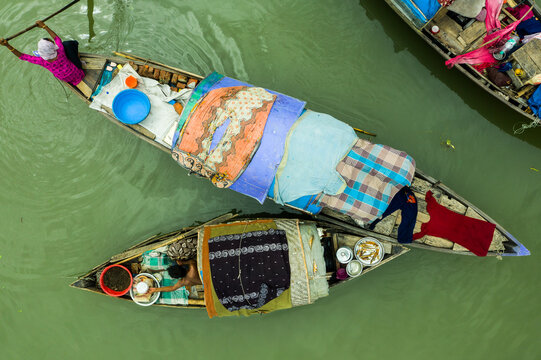 Dhaka, Bangladesh - 17 October 2021: Aerial view of traditional wooden boats carrying people and household goods along a canal in Kaderabad Housing, with calm green water.