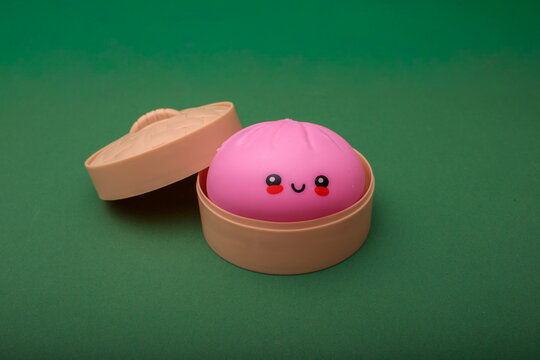 pink kawaii squishy dumpling toy in toy bamboo steamer basket with lid open beside it on green background