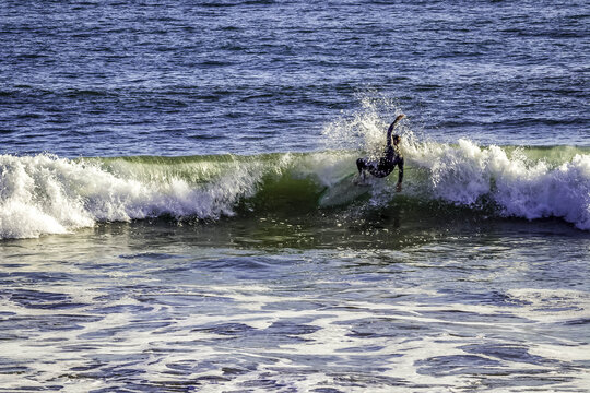 Santa Monica, United States - 07 October 2018: Aerial view of a surfer riding a wave at Santa Monica Beach with splashing water and blue ocean swells.