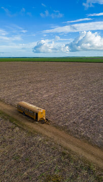 Boca de Yuma, La Altagracia Provinc, Dominican Republic - 12 September 2026: Aerial view of a yellow bus parked on a dirt path in a vast harvested agricultural field.
