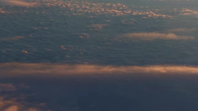A serene view above the clouds during an airplane flight, depicting a golden sunrise shedding light on the fluffy, dense cloud formations below