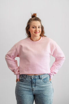 Woman keeps hand on hip wearing pastel sweatshirt and blue jeans, fashion built on soft pastel palette, essential piece of every wardrobe. Wide shot. Concept of fashion basic in pastel wardrobe