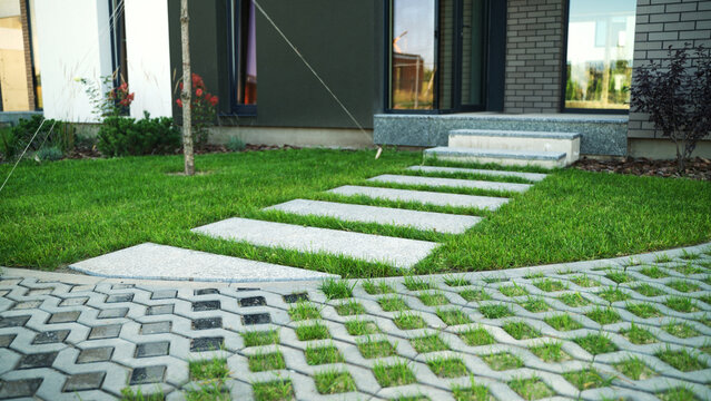 Architectural landscape showcasing modern home entrance with stepping stones and permeable pavement in lush green grass