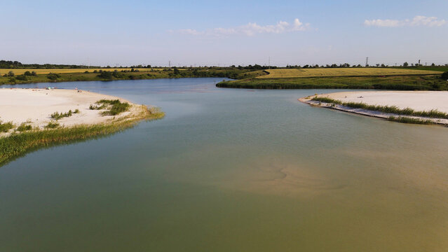 Calm river waters blending with white sand beaches. Green reeds line the banks, surrounded by vast agricultural fields on a sunny day
