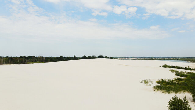 White sand dunes extending towards a lush green forest line and a distant river under a clear blue sky