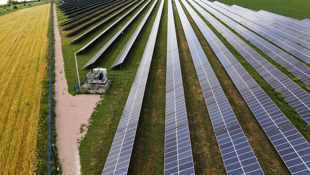 Solar farm with multiple rows of photovoltaic panels on green grass, generating clean and renewable energy near a field of crops