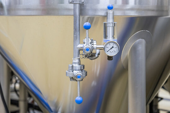 Close up of pressure gauge with valves and pipes on stainless steel tank at brewery