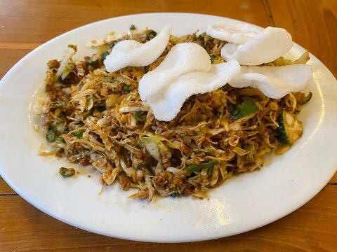 Indonesian traditional mixed vegetable salad with spicy peanut sauce topped with crunchy white crackers served on a white plate