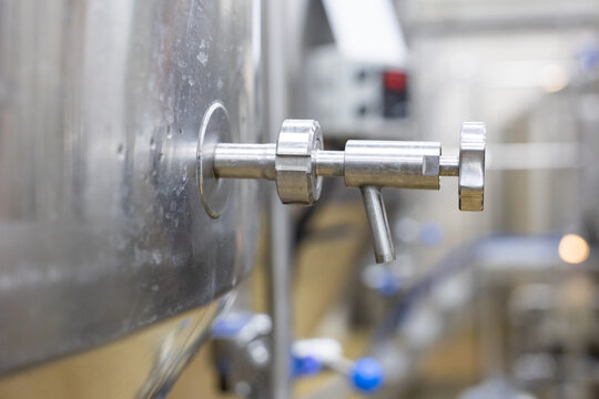 Close up of stainless steel tap on brewery tank with brewing equipment in blurred background