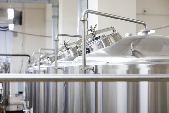 Row of stainless steel brewing tanks with pipes inside brewery production facility