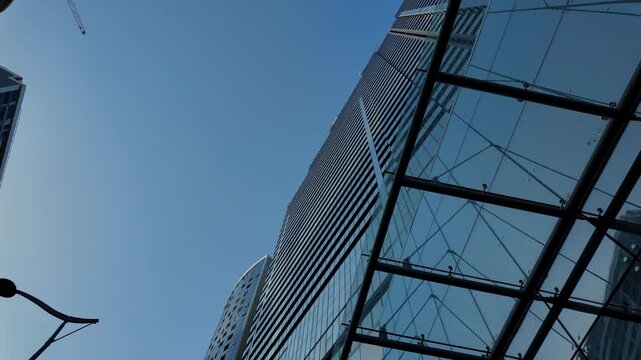 Dynamic low-angle view of a contemporary glass skyscraper facade, with its reflective windows mirroring the clear blue sky and adjacent buildings in a modern financial district on a sunny day