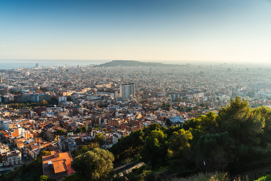 Barcelona, Spain - 01 December 2025: Aerial view of the sprawling cityscape of Barcelona, featuring dense urban architecture, terracotta rooftops, and the distant coastline under a clear sky.