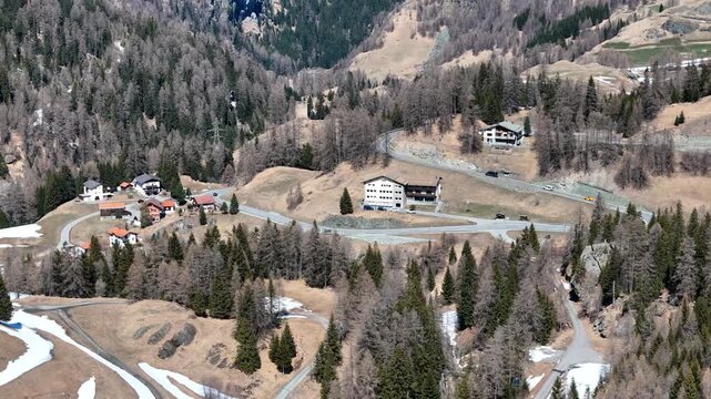 chalet rooftops alpine hamlet hairpin road loop parked cars pine forest snow patches mountainside marmorera resettled village graubunden switzerland julier pass drone footage elevated view