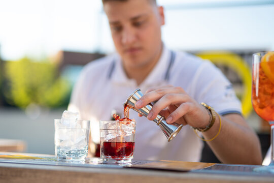 Bartender using a jigger to pour spirits into a red cocktail at an outdoor bar