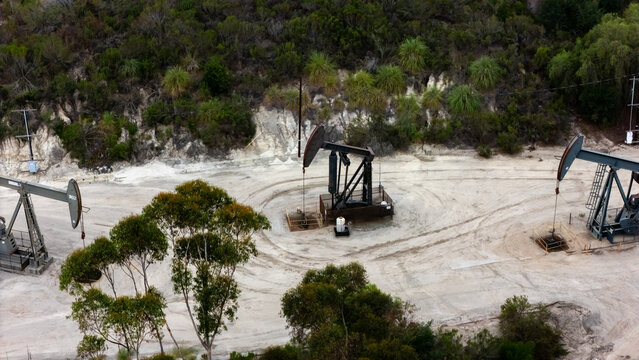 Aerial view of oil pump jacks operating in the Baldwin Hills area surrounded by dry terrain and trees in Los Angeles, California, United States.