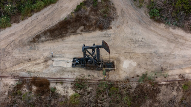 Aerial view of an oil pump jack operating in the Baldwin Hills area, surrounded by dirt paths and sparse vegetation in Los Angeles, California, United States.