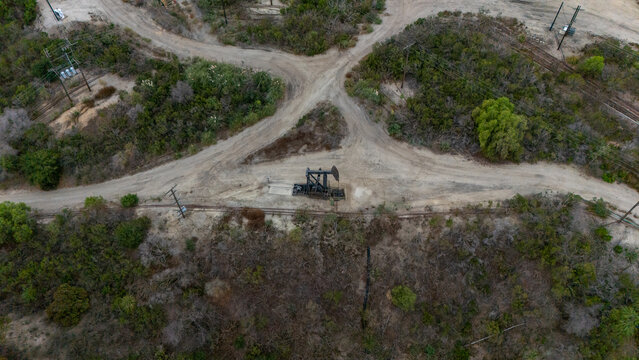 Aerial view of an oil pump jack situated in the Baldwin Hills area, surrounded by dirt roads, sparse vegetation, and power lines in Los Angeles, California, United States.