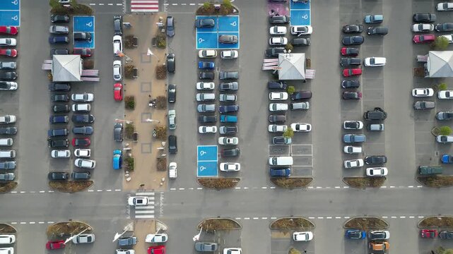 Aerial view of busy parking lot near shopping center, showcasing various vehicles in organized rows, with gradual camera zoom out revealing scene dynamics and spatial arrangement