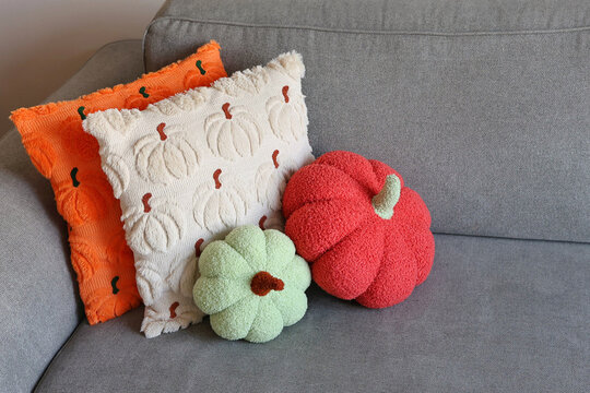 Two pumpkin-shaped cushions and textured pumpkin pillows on a gray sofa. Concept of autumn home decor and cozy fall accents.