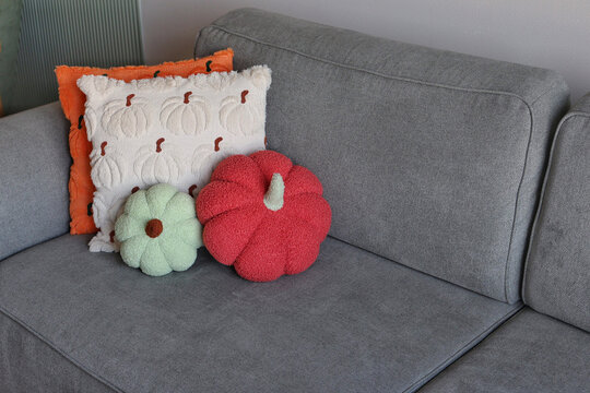 Decorative pumpkin pillows paired with two plush pumpkin cushions on a gray sofa. Concept of seasonal whimsical comfort.