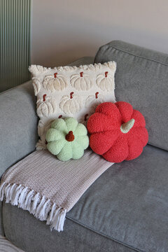 A cream pumpkin-patterned throw cushion with two plush pumpkin-shaped pillows arranged on a gray sofa.
Concept of playful autumn soft decor.