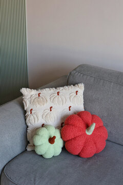 A cozy arrangement of pumpkin-themed throw pillows and plush gourds on a gray couch. Concept of autumn warmth and seasonal accents.