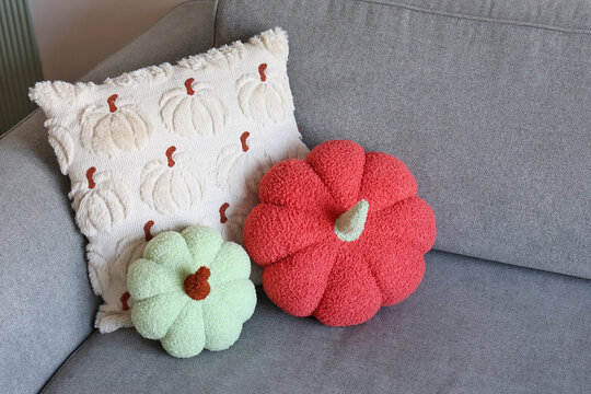 Two pumpkin-shaped plush cushions paired with a textured pumpkin throw pillow on a gray sofa.
Concept of cozy seasonal accents.